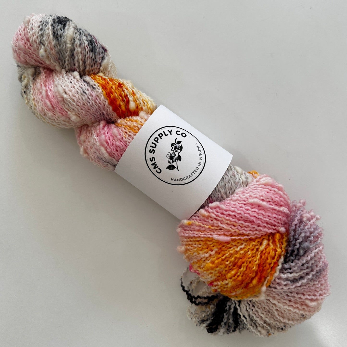 Multicolored skein of yarn with a label on a light gray background