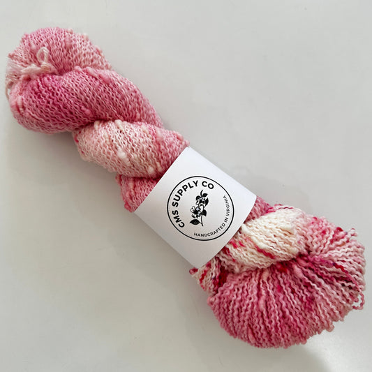 Pink skein of yarn with a label on a white background