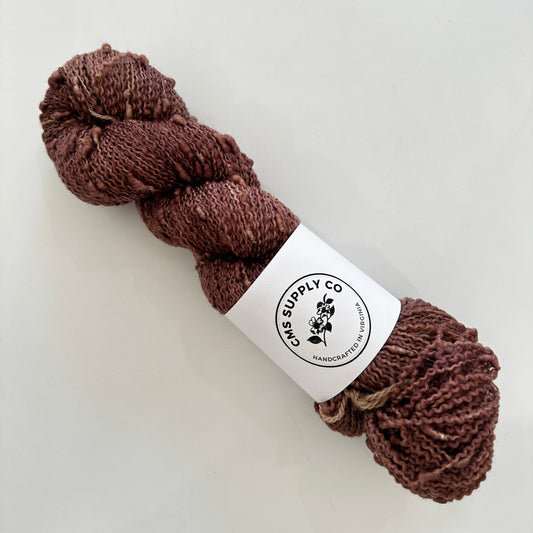 Brown skein of yarn with a label on a white background
