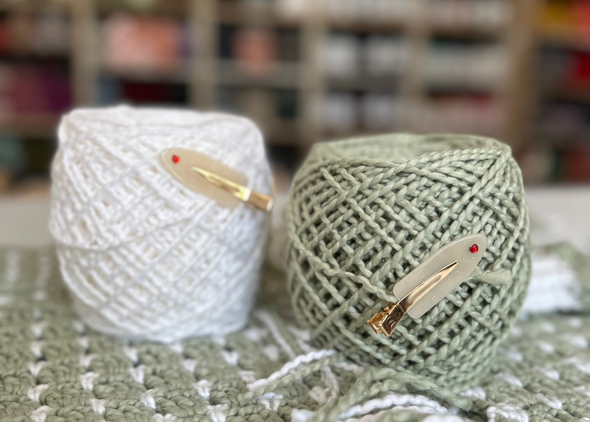 Two balls of yarn with knitting needles on a textured surface with blurred bookshelf background